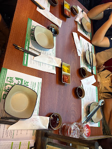 A wooden dining table set for multiple guests with white ceramic bowls, chopsticks, napkins, small condiment dishes, and menus. Two people are seated 