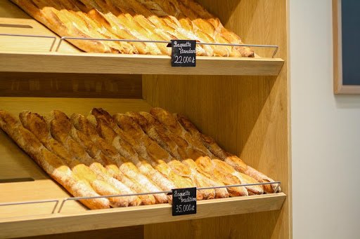 The image shows a bakery display case in Thao Dien, Saigon, featuring shelves with various types of bread and pastries labeled with prices.