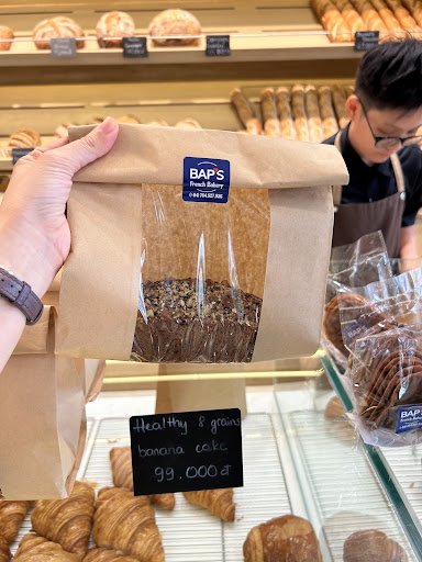 The image shows a bakery display case in Thao Dien, Saigon, featuring various baked goods such as banana cake and croissants on sale.