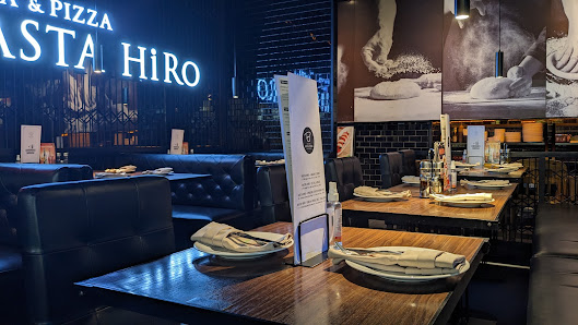 The image shows an interior view of a modern restaurant named 'PASTA HiRO'. The decor includes dark leather seating, wooden tables with neatly arrange