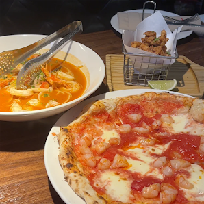 The image shows a plate of pizza topped with shrimp and cheese on the right side, alongside a bowl containing what appears to be Thai-style soup with