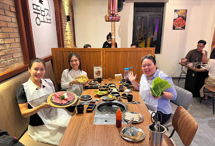 A group of people are seated at a wooden table in a restaurant, enjoying a meal. The table features a hot pot setup with various dishes, including a l