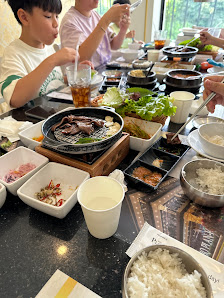 A group of people dining at a restaurant table in Thao Dien, Saigon. The table is set with various dishes including a central hot pot or grill with me