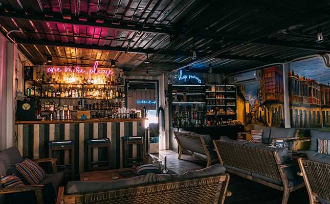 This image depicts an interior view of a bar or lounge area named 'One Mile Place'. The space features exposed brickwork, neon signs with phrases like