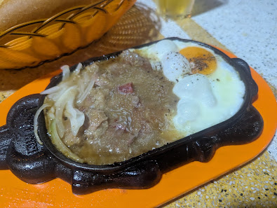 A dish served in a cast iron skillet on an orange plate features what appears to be beef stew with onions and possibly potatoes, topped with two fried