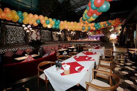 The image depicts an indoor dining area adorned with colorful balloons in the ceiling and a mix of seating arrangements including booths and chairs ar