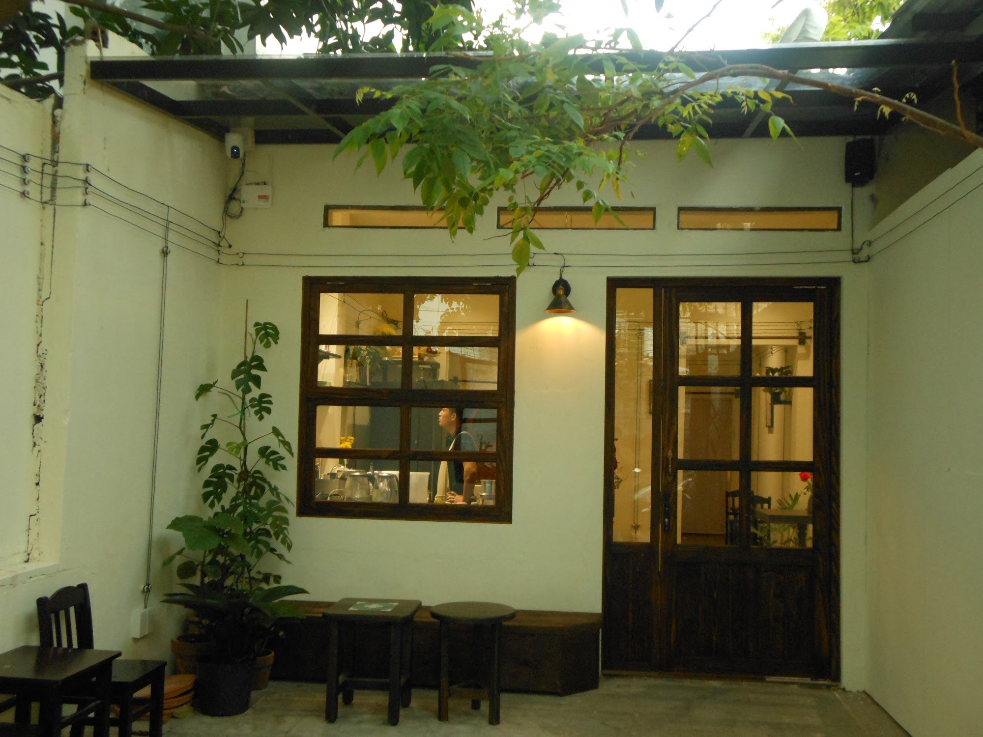 The image shows an exterior view of a cozy restaurant or café in Thao Dien, Saigon. The establishment has wooden doors and large windows with visible 