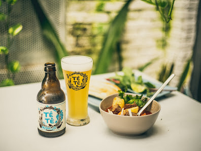 The image shows a bottle of 'Te Tê' beer and a glass filled with the same beverage alongside a bowl containing what appears to be noodle soup, garnish