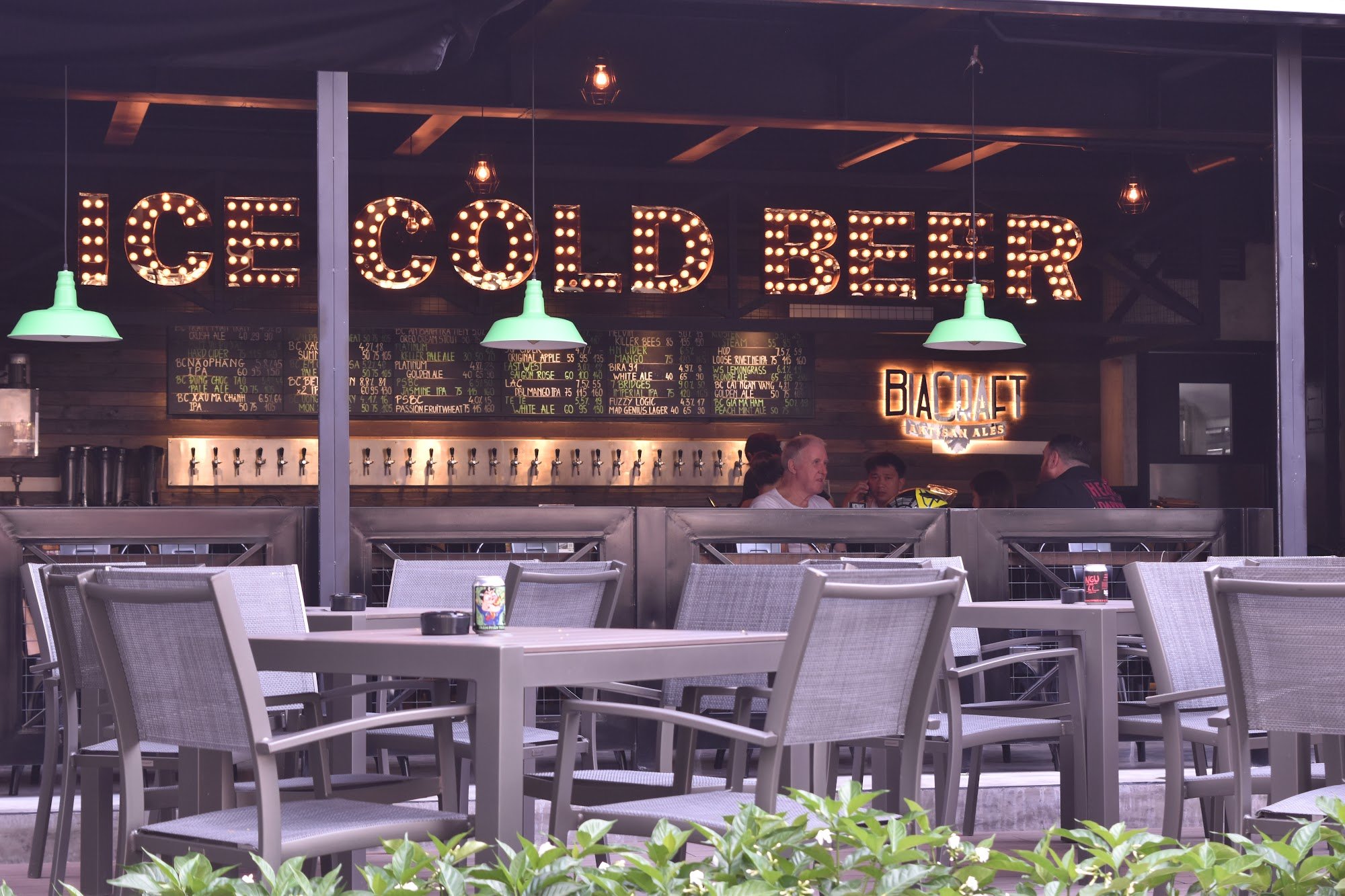 Outdoor patio of a beer venue in Thao Dien, Saigon. Features large illuminated "ICE COLD BEER" sign, a menu board listing various beers, "BIACRAFT" br