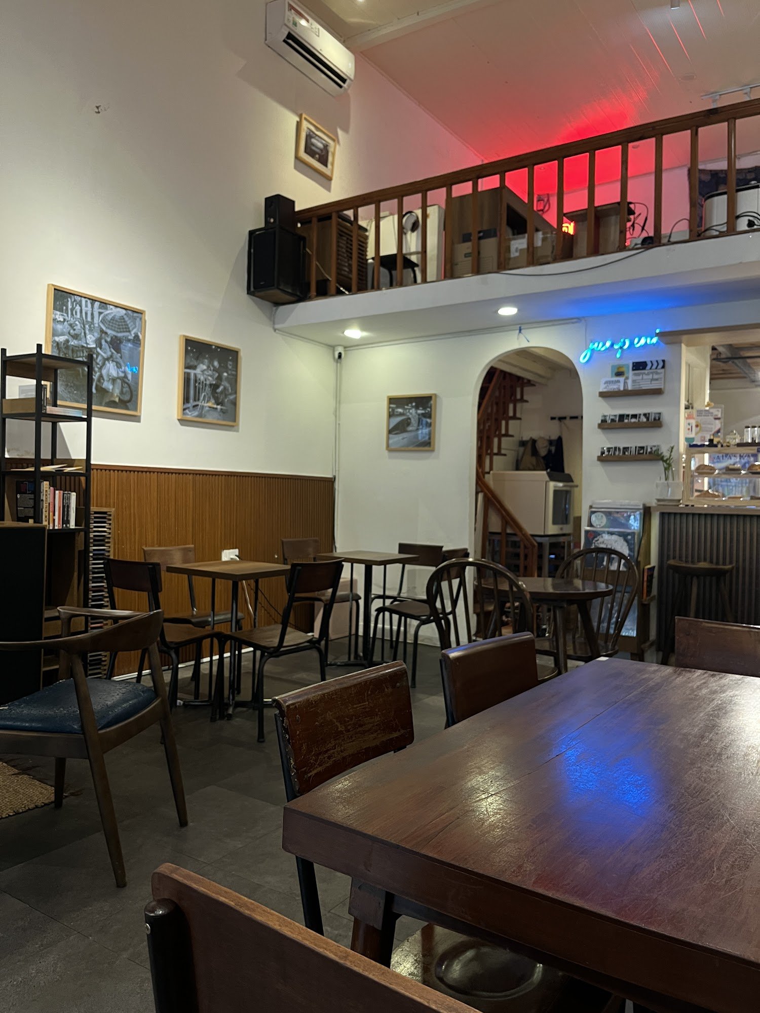 The image shows an interior view of a cozy café or restaurant in Thao Dien, Saigon. The space features wooden tables and chairs with various seating a