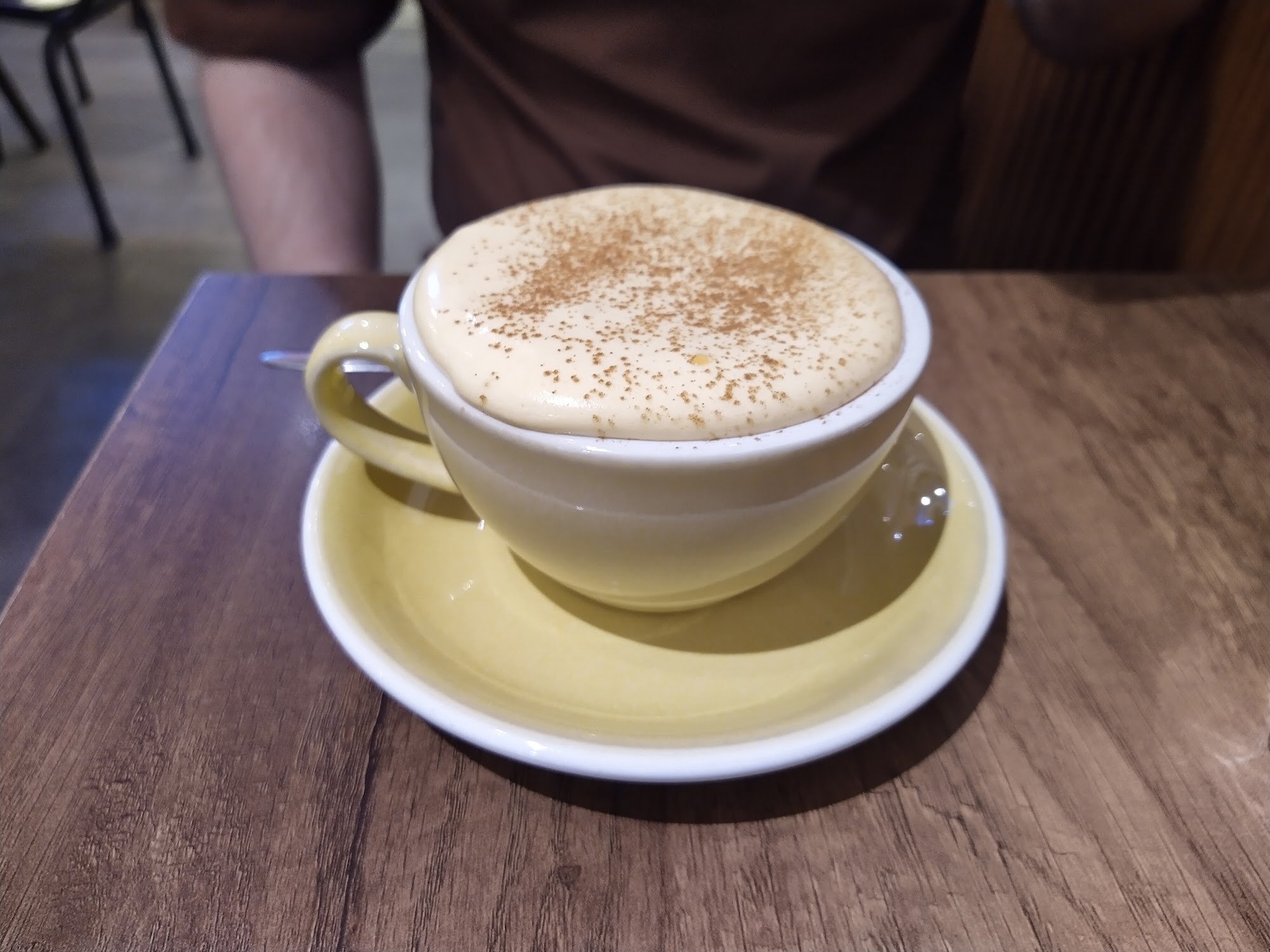 A close-up of a cappuccino served in a yellow cup and saucer on a wooden table.