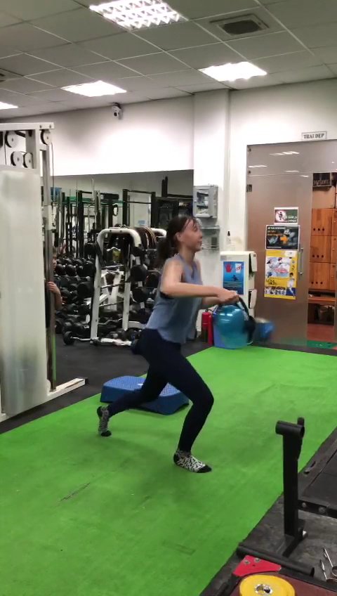 A woman is exercising in a gym setting with various fitness equipment and green flooring.
