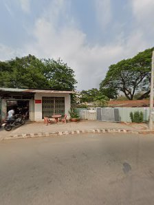 The image shows an exterior view of a small building or shop located on the side of a road with trees and greenery in the background.