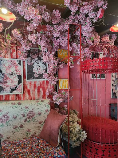 This image depicts an interior space that appears to be a café or lounge area decorated with vibrant pink cherry blossom flowers covering the ceiling 