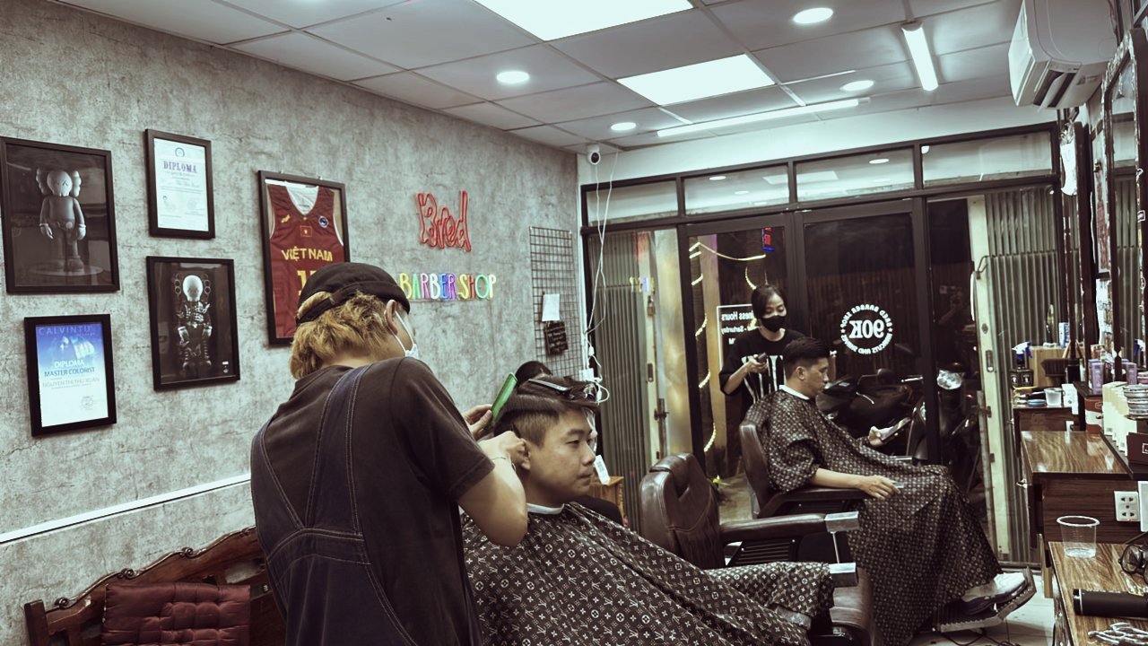 The image depicts an interior view of a barber shop named 'Bored Barber Shop'. A customer is seated in the foreground, receiving a haircut from a barb