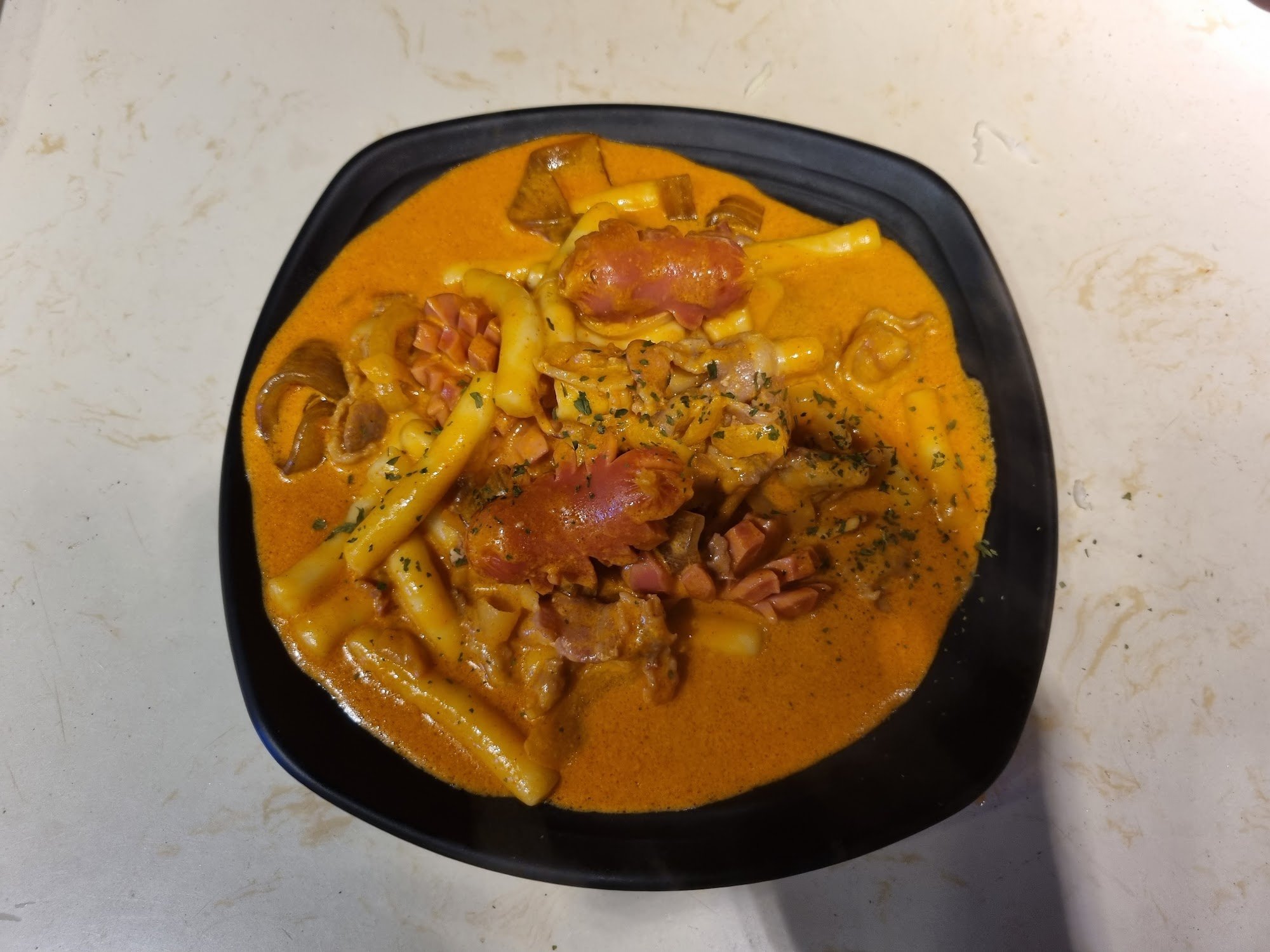 A bowl of creamy orange pasta dish garnished with pieces of sausage and mushrooms.