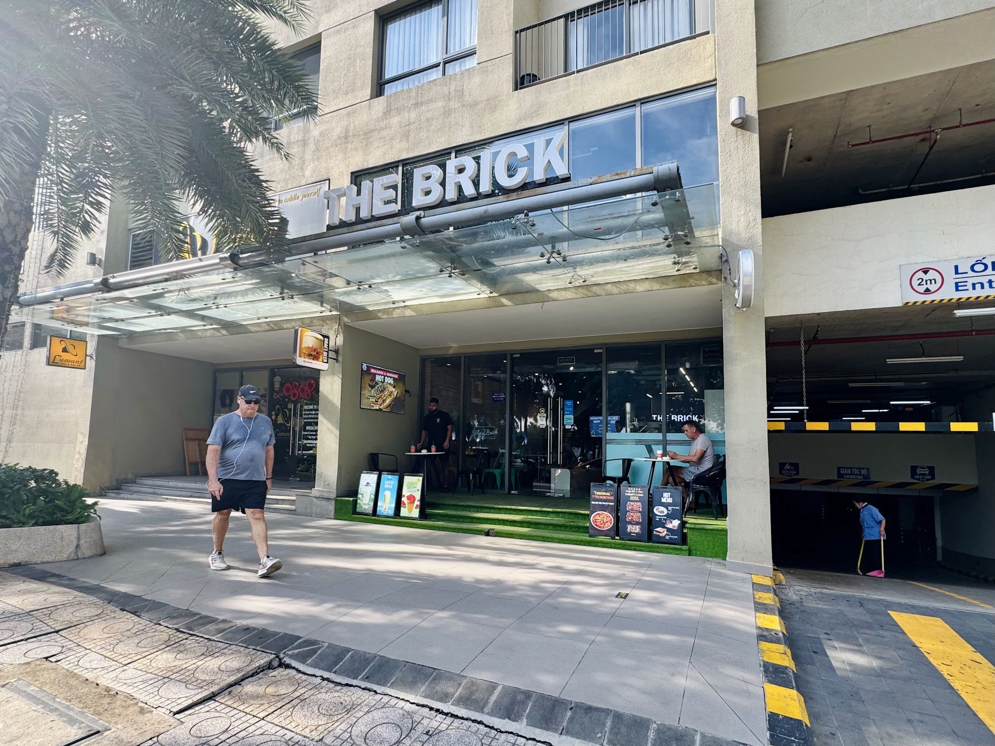 The image shows an exterior view of a restaurant named 'THE BRICK'. The establishment has large glass doors and windows, with outdoor seating visible