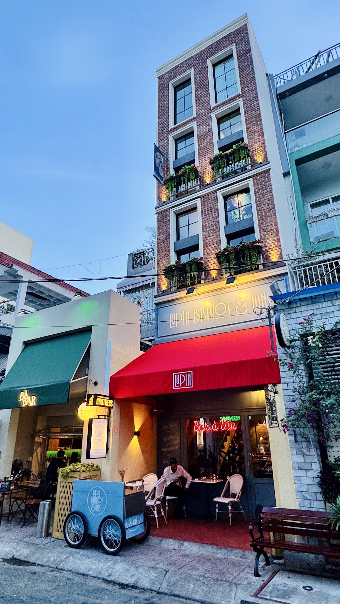 The image shows an exterior view of a restaurant named 'UPIN BISTRO & WIN' with outdoor seating visible in the foreground, including tables and chairs