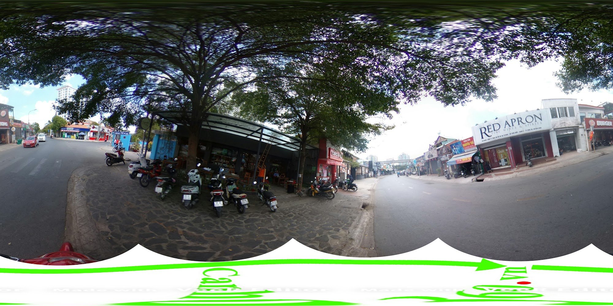 The image depicts a bustling street scene in Thao Dien, Saigon, featuring a curved road with parked motorbikes under shaded areas with large trees. On