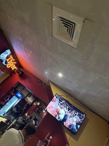 The image shows an interior view of a restaurant or bar named 'Tiger' with neon signage on the left side, and patrons seated at tables watching a boxi