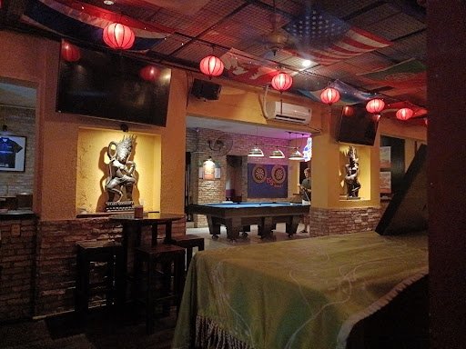 The image depicts the interior of a venue in Thao Dien, Saigon. It features a central pool table surrounded by brick walls. Red lanterns hang from the