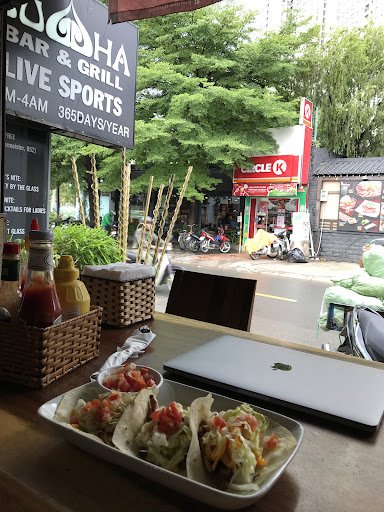The image depicts an outdoor seating area of a bar and grill venue in Thao Dien, Saigon. On the table, there's a white tray with several tacos or simi
