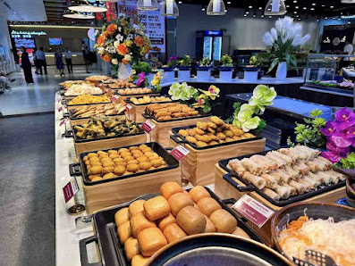 A well-organized buffet display in a modern indoor venue in Thao Dien, Saigon. The image features multiple trays of various food items including sprin