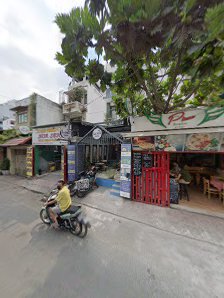 The image shows a street view of an area in Thao Dien, Saigon with various shops and eateries on the side. A person is riding a motorcycle past one su
