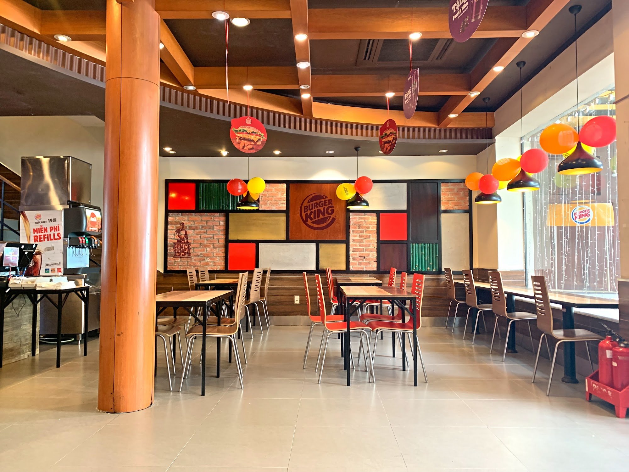 The image shows an interior view of a Burger King restaurant located in Thao Dien, Saigon. The decor features wooden beams on the ceiling and walls wi