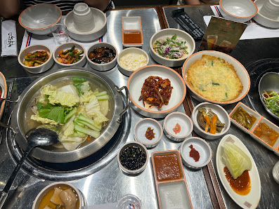 A variety of Korean dishes including a hot pot, kimchi, various side dishes like pickled vegetables and sauces
