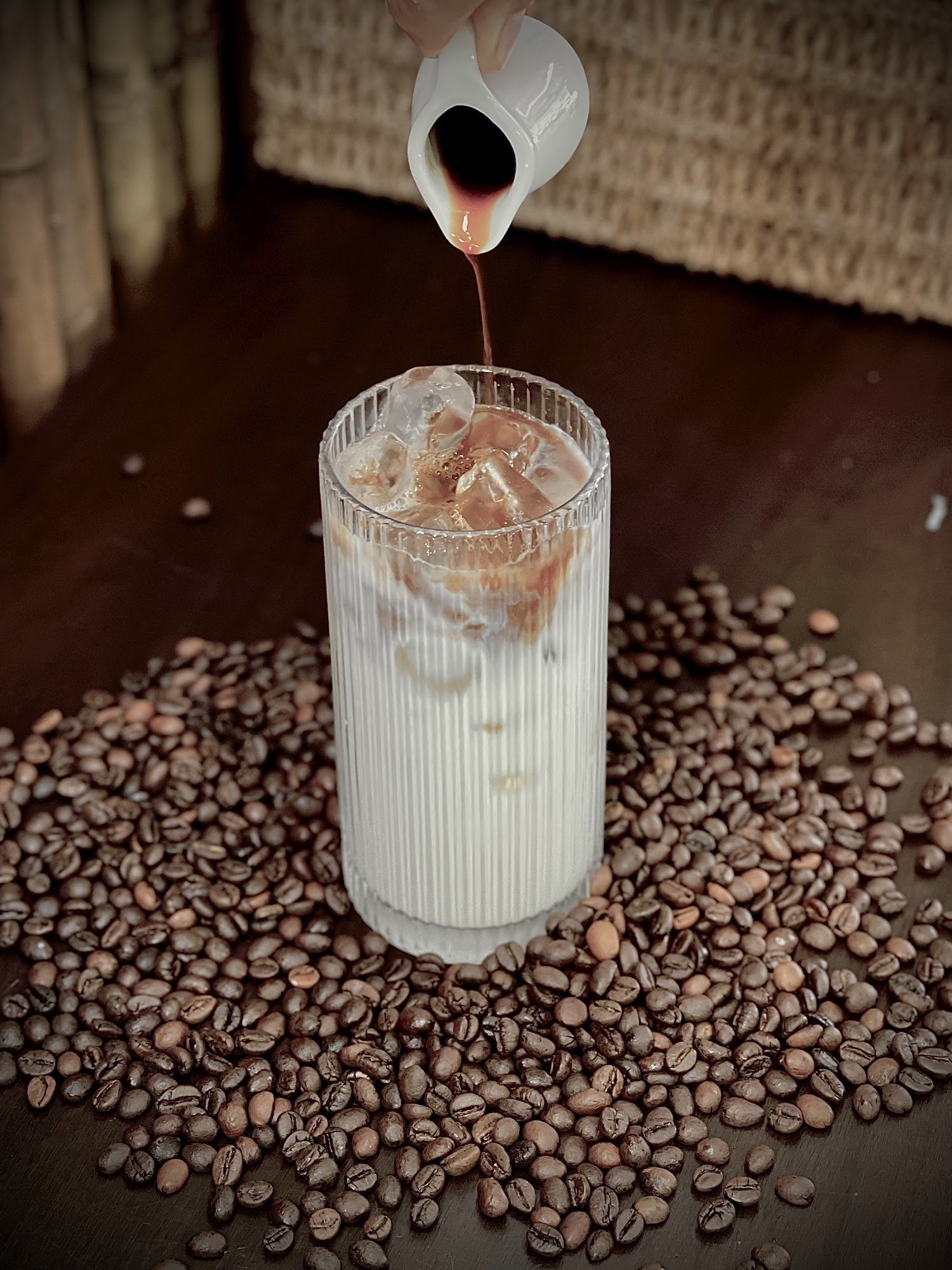 A close-up shot of a glass being filled with an iced coffee beverage as it is poured from a small jug into the cup, which already contains ice cubes a