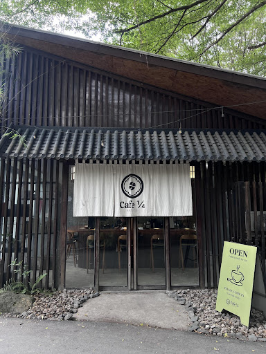 The image shows an exterior view of a cafe named 'Cafe 1/2' with wooden slat walls and a tiled roof, featuring large glass doors that are currently op