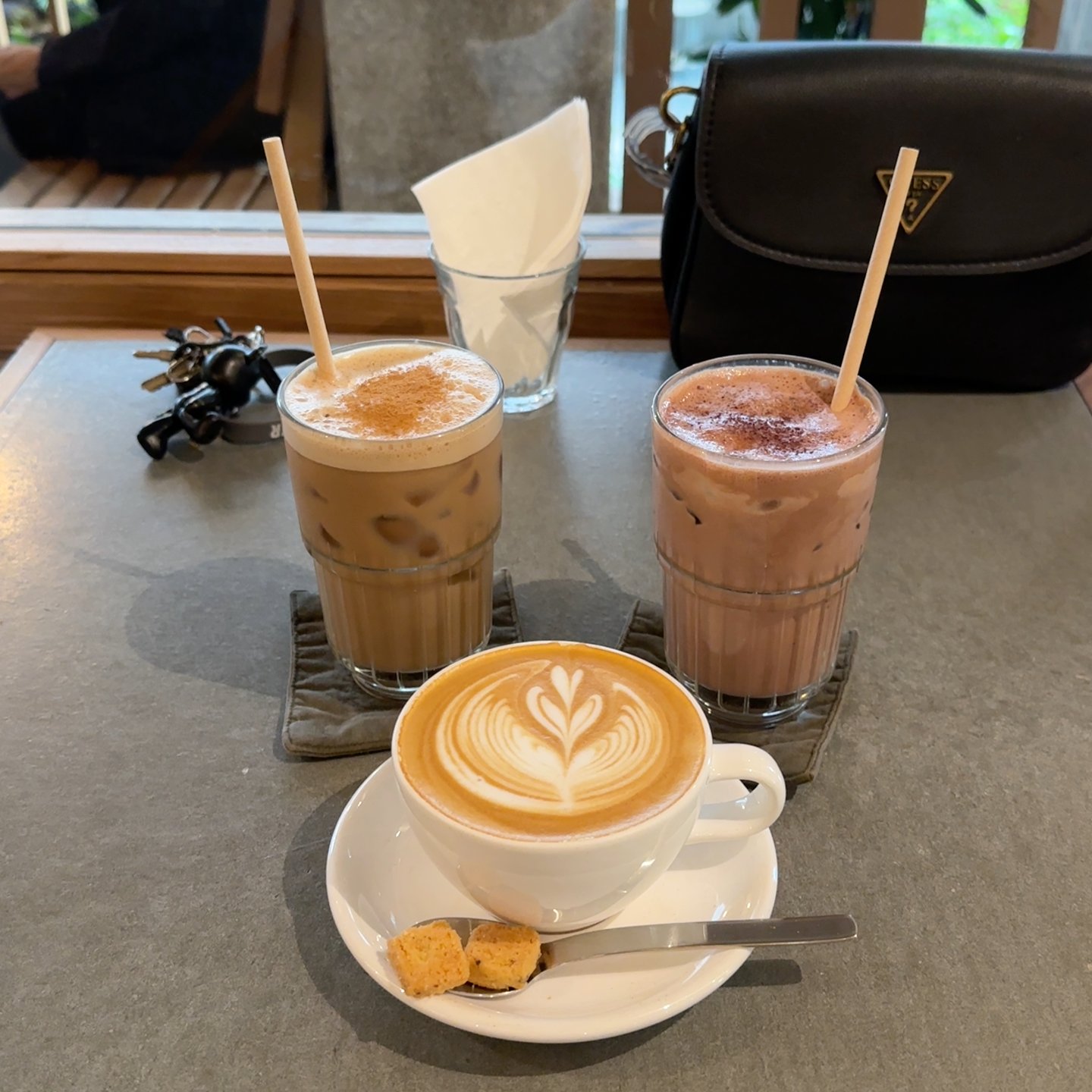 The image shows a table in an indoor setting at Thao Dien, Saigon with three cold beverages and one cup of coffee on it.