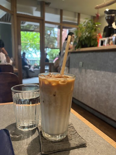 A glass of cold coffee beverage on a table in an indoor setting that appears to be a cafe or restaurant with natural light coming through the windows 