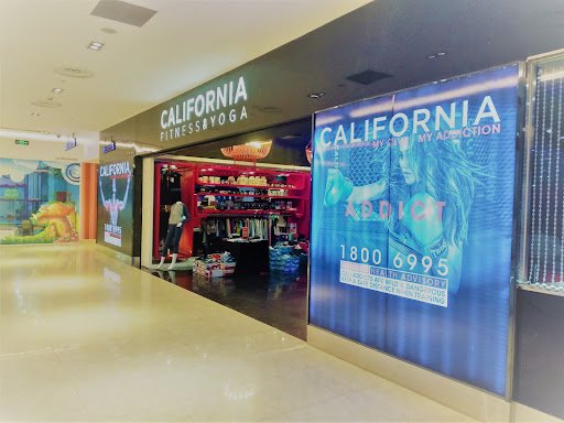 The image shows an interior view of a shopping mall featuring the California Fitness & Yoga store with various promotional banners and displays.