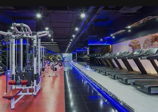 The image shows a modern gym interior featuring various exercise equipment such as treadmills and weight machines. The flooring is reflective, possibl