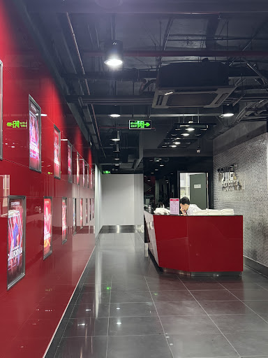 The image shows an indoor setting that appears modern and clean, featuring a red reception desk with a person working behind it. The walls are adorned
