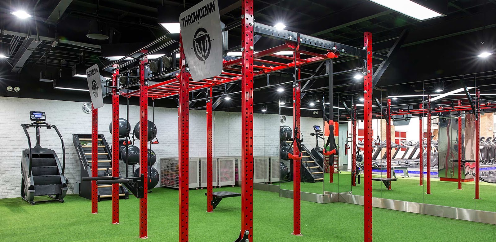The image shows an indoor gym facility equipped with various exercise machines and equipment such as treadmills, elliptical trainers, medicine balls,