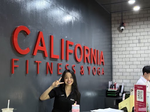 The image shows an interior view of a fitness and yoga studio named 'California Fitness & Yoga'. A staff member is posing in front of the wall with th