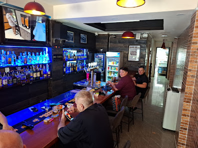 The image shows an interior view of a bar or pub setting in Thao Dien, Saigon. Patrons are seated at the counter with various bottles and glasses visi