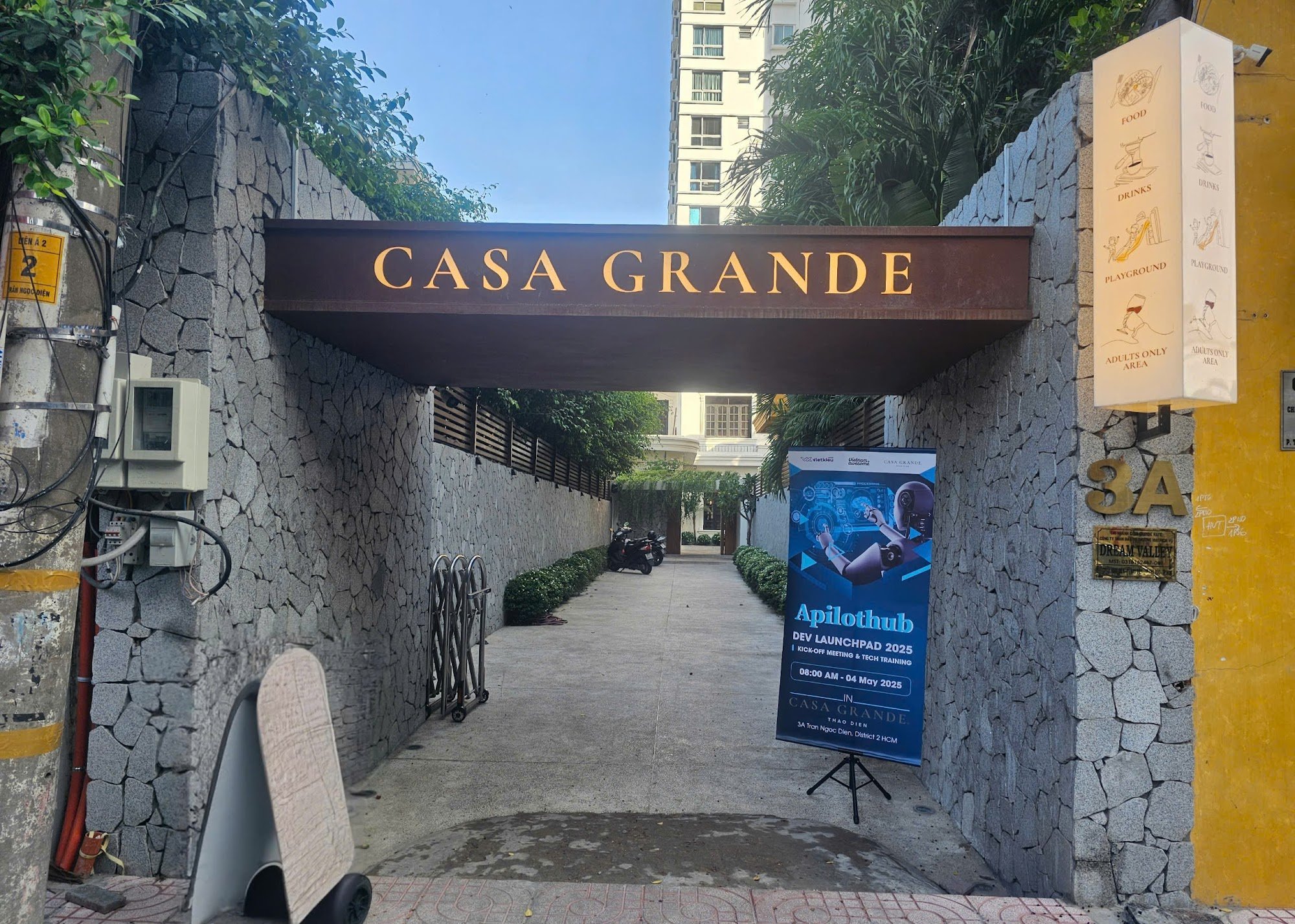 The image shows an entrance gate labeled 'CASA GRANDE' leading into a residential complex with stone walls and greenery on either side.