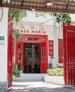 The image shows an exterior view of a building named 'Casa Maria'. The entrance is marked by vibrant red doors and gates, with the name prominently di