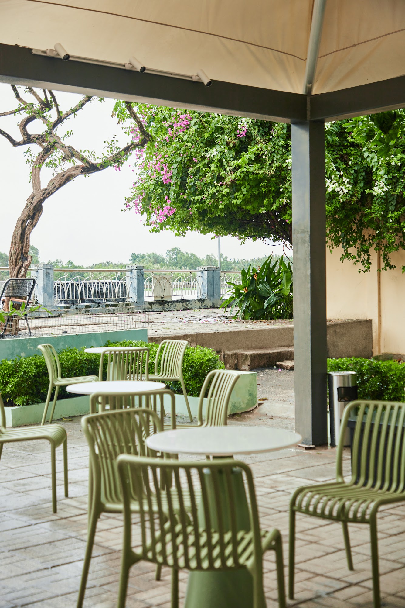 The image shows an outdoor seating area of a venue in Thao Dien, Saigon. The setting includes green chairs and tables under a beige canopy with white 