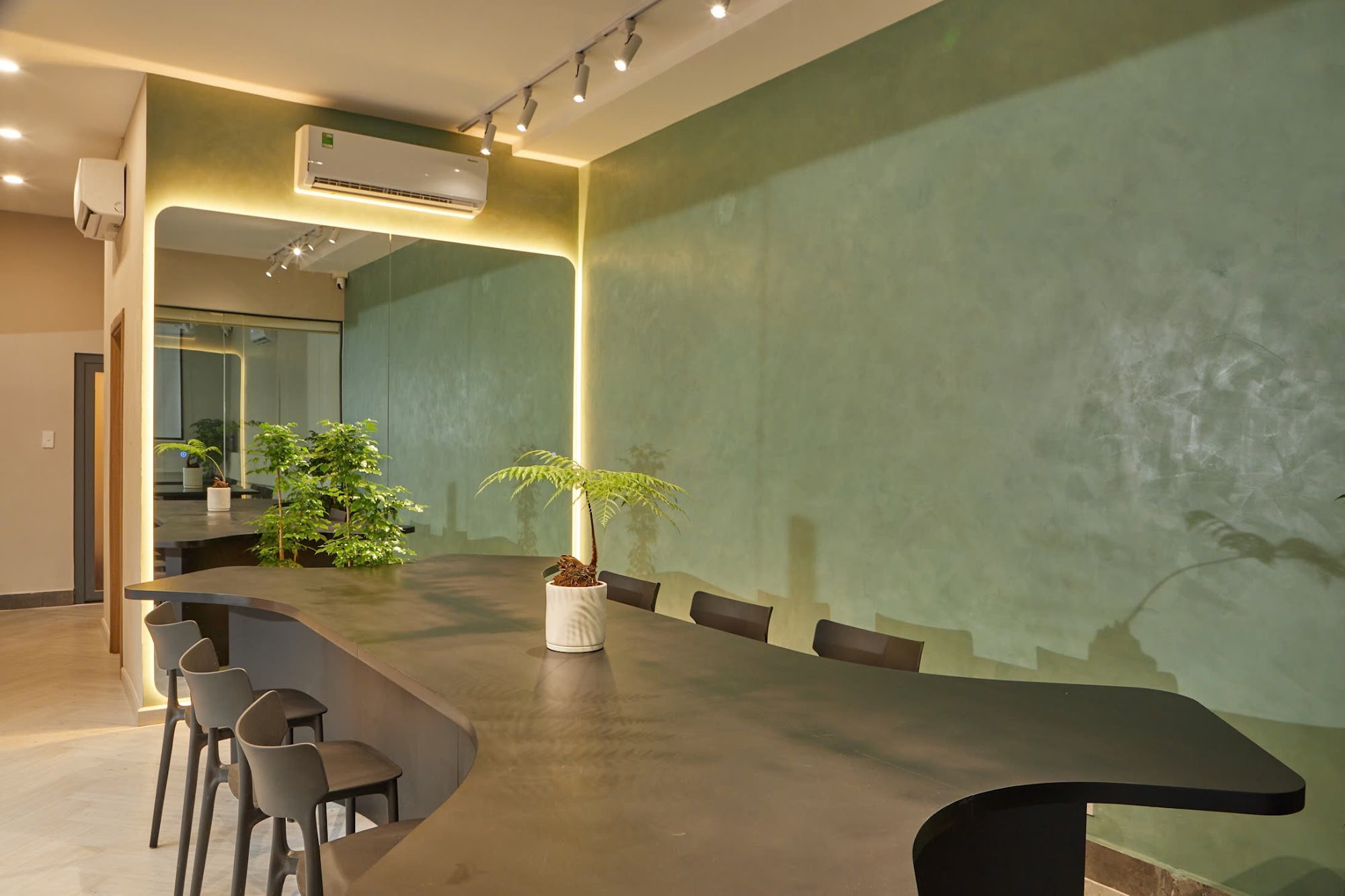 This image depicts a modern interior space featuring an L-shaped bar counter in the foreground with dark grey chairs and stools around it, leading to 