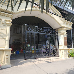 The image depicts the exterior entrance of a venue in Thao Dien, Saigon. It features an ornate black iron gate with intricate scrollwork, flanked by c