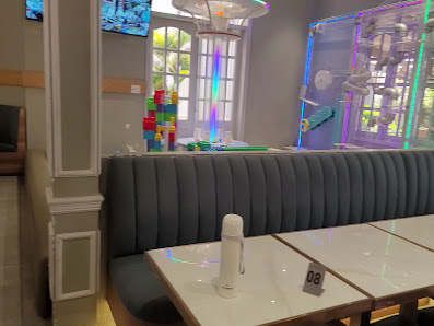 The image shows an interior view of a modern dining area featuring contemporary furniture and decor elements such as colorful LED lighting on the wall