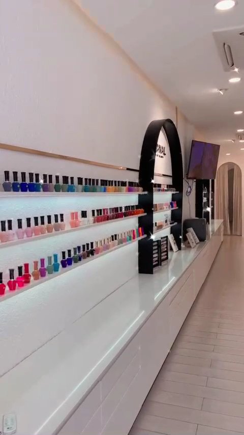 The image shows a well-lit interior of what appears to be a nail salon or beauty store with an extensive display of colorful nail polish bottles on sh
