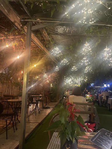 The image depicts an interior view of a restaurant or cafe at night. The space is adorned with numerous hanging lights that create a warm and inviting