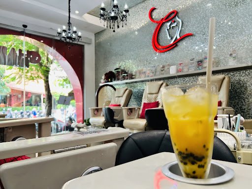 The image shows an interior view of a modern nail salon or beauty parlor. The foreground features a bright yellow drink with black pearls, likely bubb