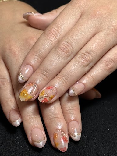 A close-up photograph of a person's hands displaying intricately designed nail art featuring autumnal colors and glittery accents.